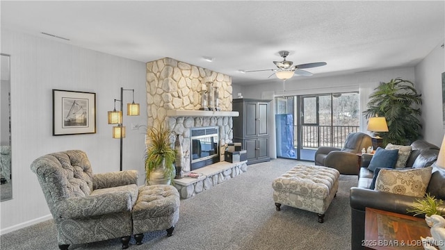 living room featuring visible vents, carpet floors, a stone fireplace, and ceiling fan