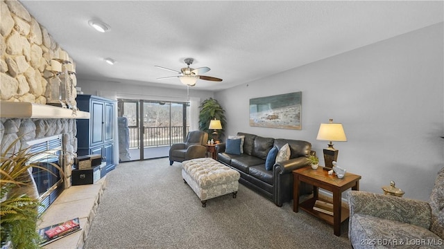 carpeted living area featuring a stone fireplace and ceiling fan