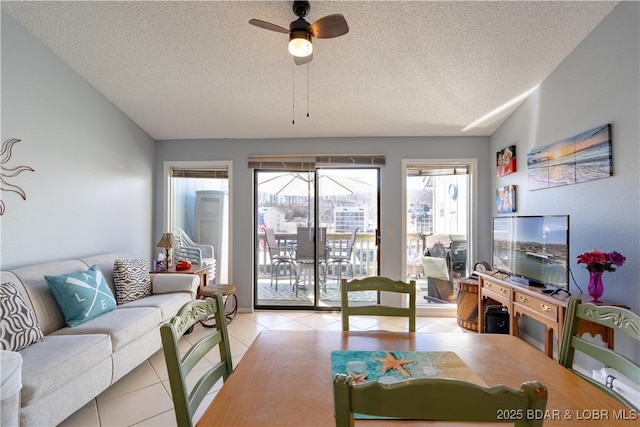 living area featuring ceiling fan, lofted ceiling, a textured ceiling, and light tile patterned flooring