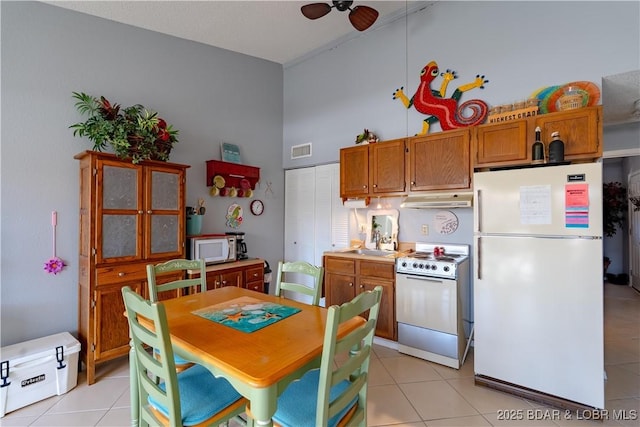 kitchen featuring visible vents, light tile patterned floors, brown cabinets, a towering ceiling, and white appliances