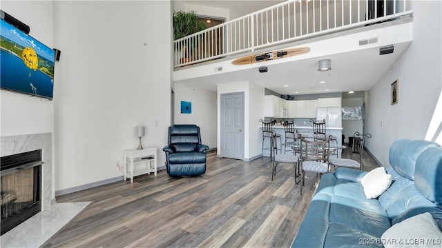 living room featuring visible vents, baseboards, a premium fireplace, a high ceiling, and wood finished floors