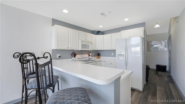 kitchen with white appliances, a breakfast bar, a peninsula, light countertops, and white cabinetry