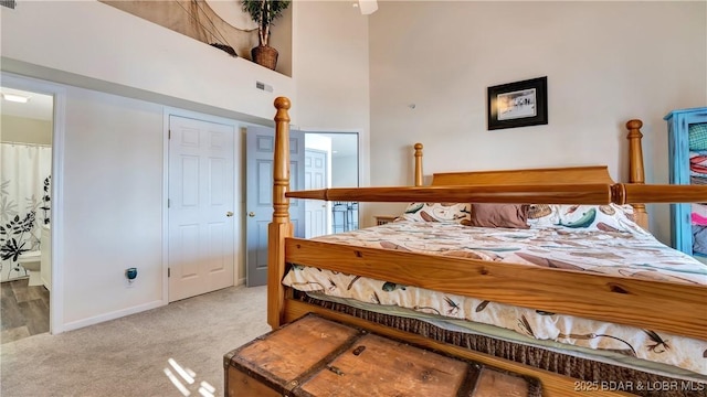 carpeted bedroom with a towering ceiling, baseboards, visible vents, and ensuite bathroom