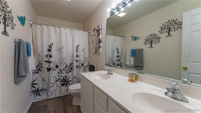 bathroom with double vanity, toilet, wood finished floors, and a sink