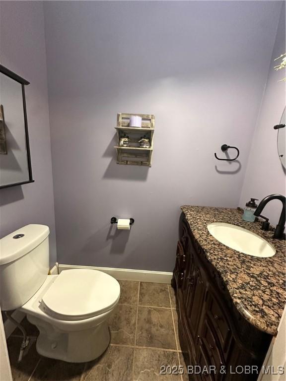 half bathroom featuring vanity, toilet, and baseboards