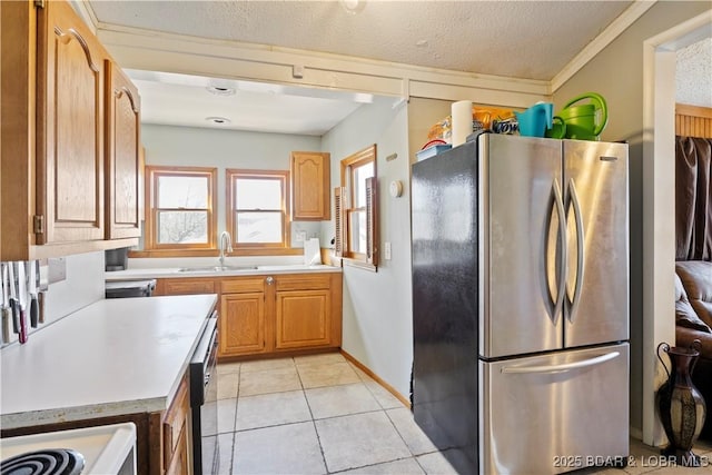 kitchen with light tile patterned floors, freestanding refrigerator, a sink, light countertops, and a textured ceiling