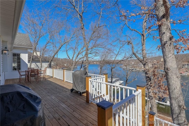 wooden deck with grilling area, a water view, and outdoor dining space