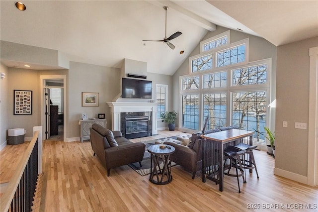 living room with a high end fireplace, beam ceiling, light wood-style flooring, high vaulted ceiling, and a ceiling fan