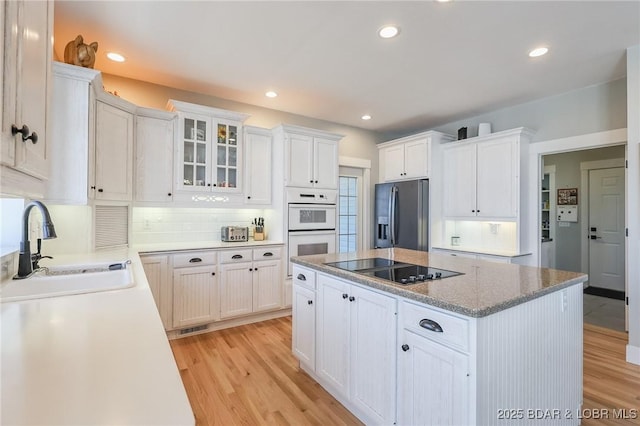 kitchen with a sink, light wood-style floors, stainless steel refrigerator with ice dispenser, black electric cooktop, and a center island