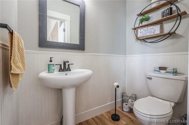 half bath featuring toilet, wood finished floors, and wainscoting