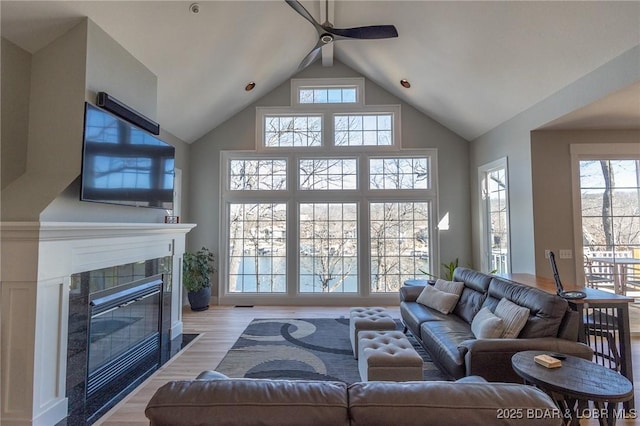 living room featuring a tiled fireplace, high vaulted ceiling, a ceiling fan, and wood finished floors