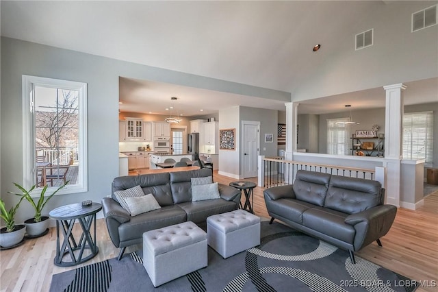 living area featuring visible vents, light wood-type flooring, and decorative columns