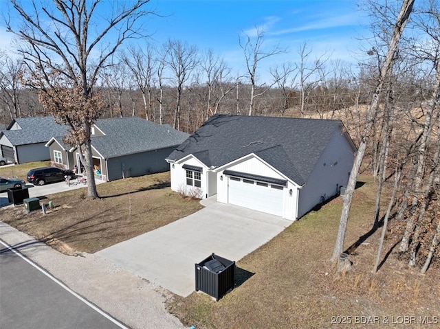 view of front facade featuring driveway, an attached garage, roof with shingles, and a front yard