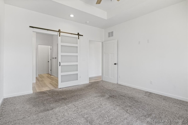 unfurnished bedroom with baseboards, visible vents, recessed lighting, a barn door, and carpet flooring