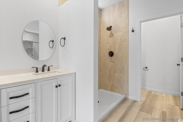 full bathroom featuring a tile shower, visible vents, vanity, and wood finished floors