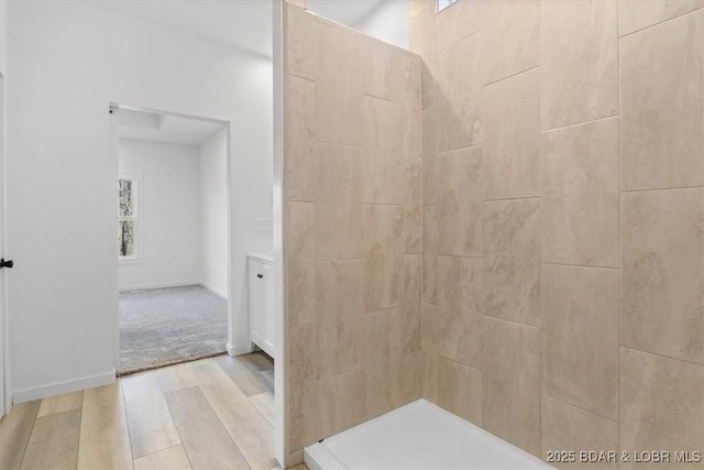 full bath with baseboards, tiled shower, and wood finished floors