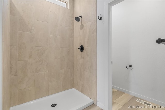 bathroom with a tile shower, visible vents, and baseboards