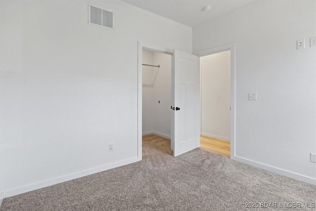 unfurnished bedroom with visible vents, a closet, carpet floors, baseboards, and a spacious closet