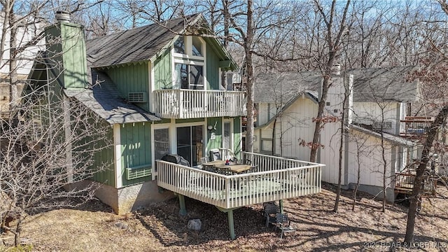 rear view of house featuring a chimney, a balcony, and roof with shingles