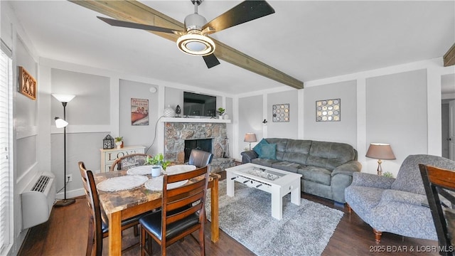 living room featuring beam ceiling, dark wood-type flooring, a wall unit AC, a fireplace, and ceiling fan