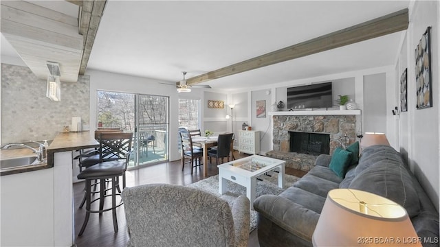 living room featuring beamed ceiling, a ceiling fan, wood finished floors, and a fireplace