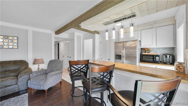 kitchen with black microwave, beamed ceiling, butcher block countertops, a breakfast bar, and stainless steel fridge