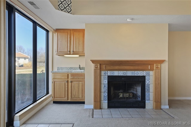 interior space with a sink, baseboards, light colored carpet, and a tile fireplace