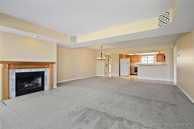 unfurnished living room featuring a fireplace, baseboards, a chandelier, and light carpet