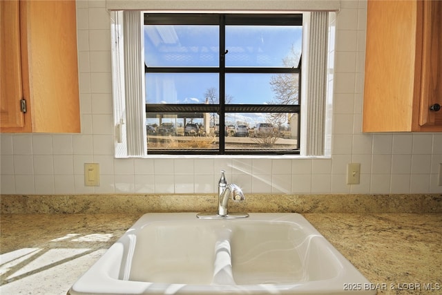 details with a sink, light stone countertops, tasteful backsplash, and brown cabinetry