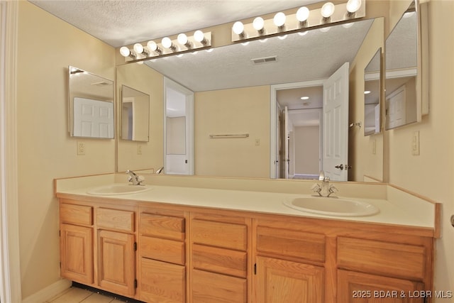 full bathroom featuring a textured ceiling, double vanity, visible vents, and a sink