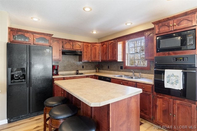 kitchen featuring light wood finished floors, a sink, black appliances, light countertops, and under cabinet range hood