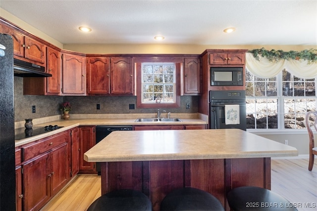 kitchen with light wood finished floors, a breakfast bar, a sink, black appliances, and light countertops