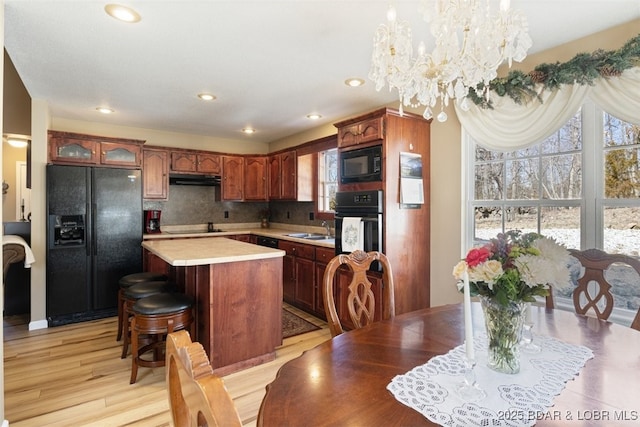 kitchen with a kitchen island, a sink, decorative backsplash, black appliances, and light countertops