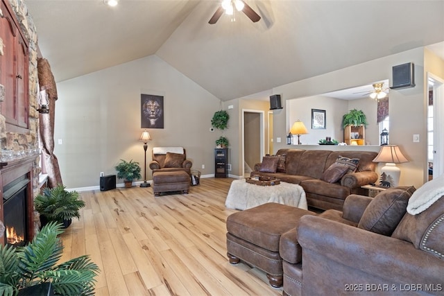 living area with baseboards, light wood finished floors, ceiling fan, vaulted ceiling, and a glass covered fireplace