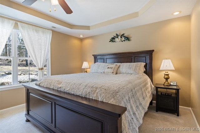 bedroom featuring visible vents, light colored carpet, a tray ceiling, and multiple windows