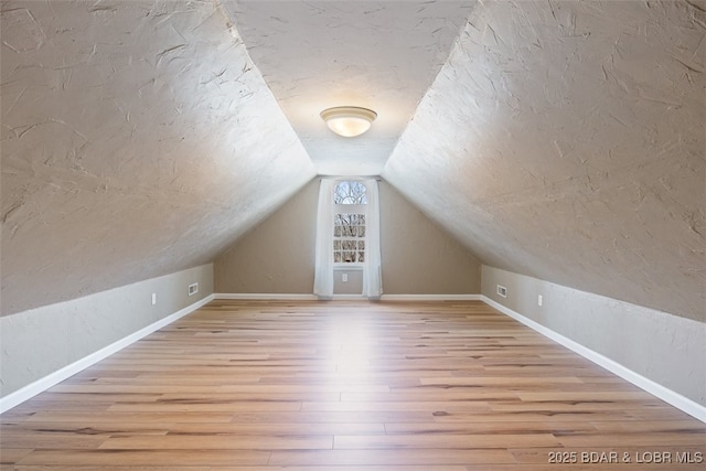 additional living space with baseboards, lofted ceiling, a textured ceiling, and wood finished floors