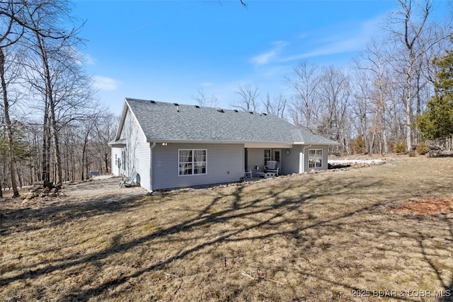 rear view of property featuring a lawn and roof with shingles