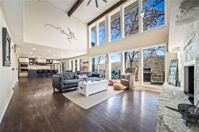 living area featuring a stone fireplace, beamed ceiling, dark wood-style floors, and a high ceiling