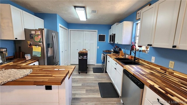 kitchen with white cabinets, visible vents, stainless steel appliances, and butcher block counters