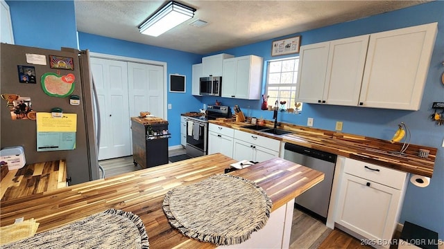 kitchen with butcher block counters, wood finished floors, white cabinets, stainless steel appliances, and a sink