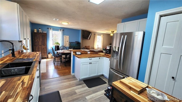 kitchen with white cabinetry, butcher block countertops, light wood-style flooring, stainless steel fridge, and a textured ceiling