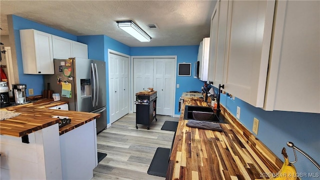 kitchen featuring visible vents, stainless steel refrigerator with ice dispenser, a sink, white cabinetry, and butcher block counters