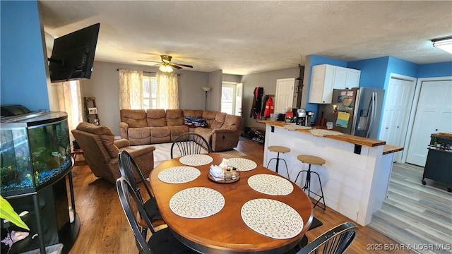 dining room with light wood-style flooring, a ceiling fan, and a textured ceiling