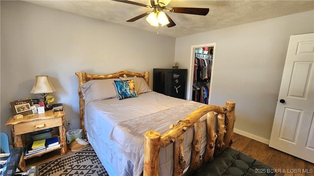 bedroom with a textured ceiling, wood finished floors, a closet, baseboards, and a spacious closet