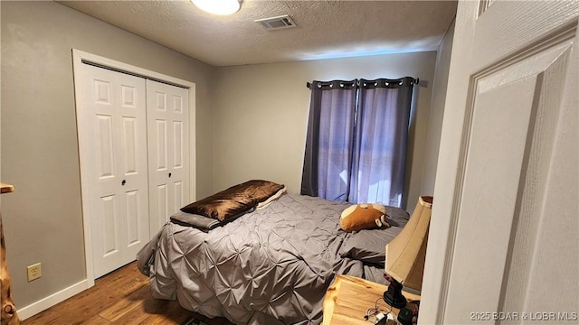 bedroom with visible vents, a textured ceiling, wood finished floors, a closet, and baseboards