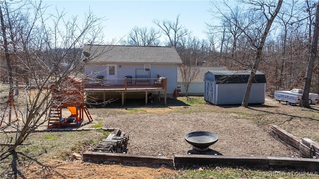 back of property featuring a deck, a playground, a shed, an outdoor structure, and a shingled roof