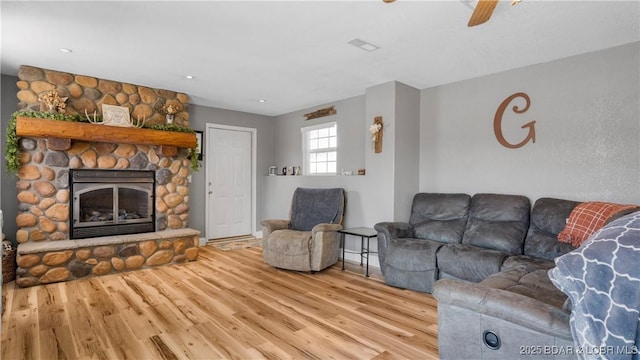 living area with a stone fireplace, visible vents, ceiling fan, and wood finished floors