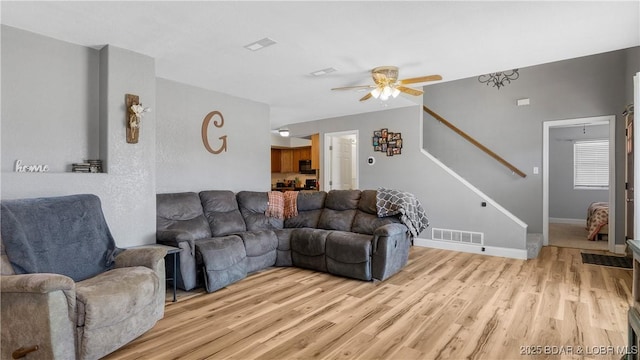 living room featuring a ceiling fan, stairway, light wood-style floors, and visible vents