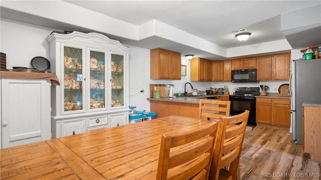 kitchen featuring visible vents, black appliances, a sink, light wood-style floors, and brown cabinetry