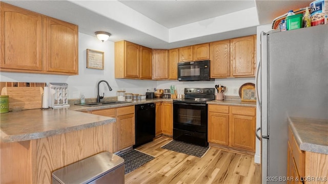 kitchen featuring light wood-type flooring, black appliances, a sink, a tray ceiling, and a peninsula